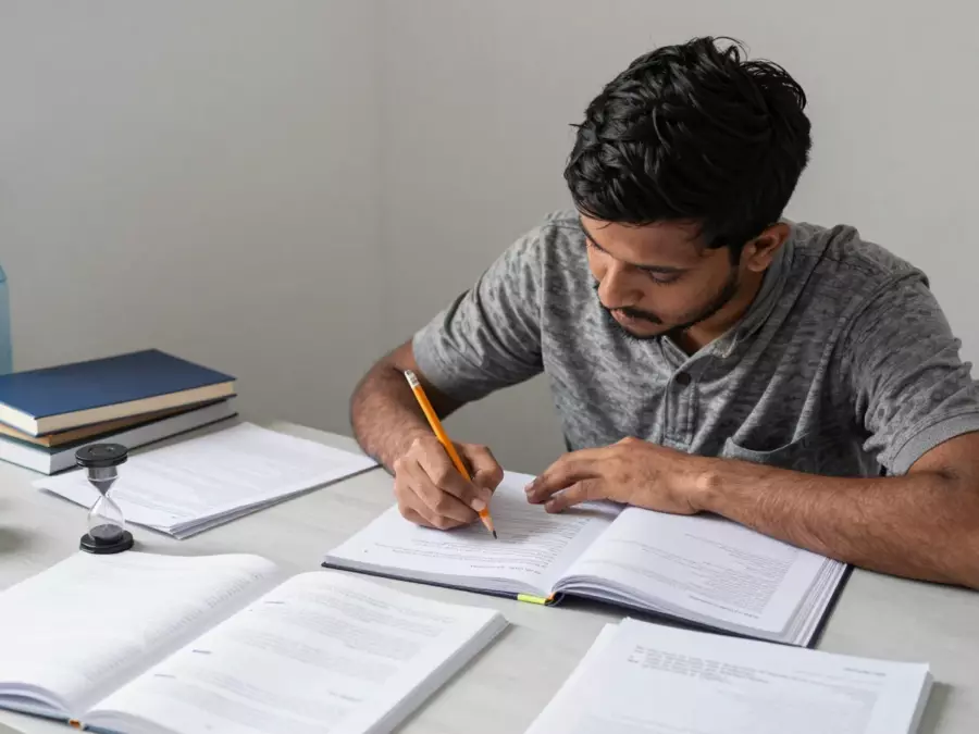 আইইএলটিএস শিক্ষার্থী সময়মতো উপকরণ সহ পড়া এবং লেখা শোনার অনুশীলন করছে