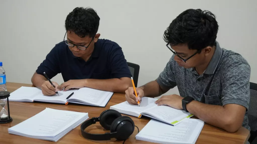 Siswa menjalankan tes latihan IELTS dengan catatan, headphone, dan pengatur waktu