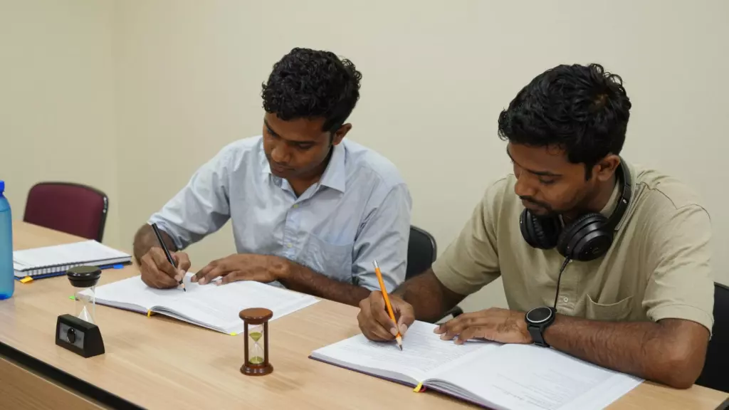 குறிப்புகள், ஹெட்ஃபோன்கள் மற்றும் டைமருடன் IELTS பயிற்சி சோதனையை நடத்தும் மாணவர்