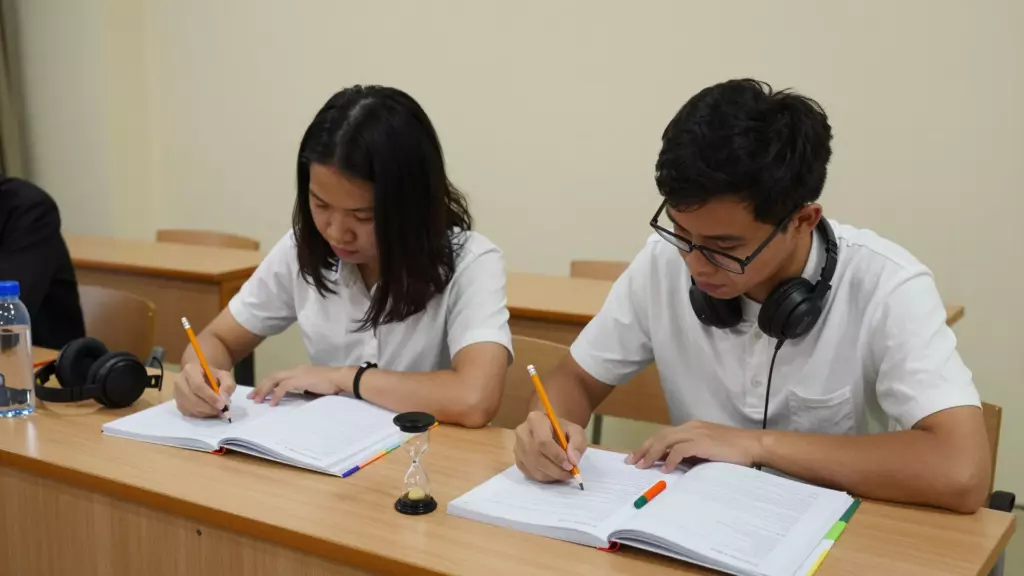 Học viên thực hiện bài kiểm tra thực hành IELTS bằng ghi chú, tai nghe và đồng hồ bấm giờ